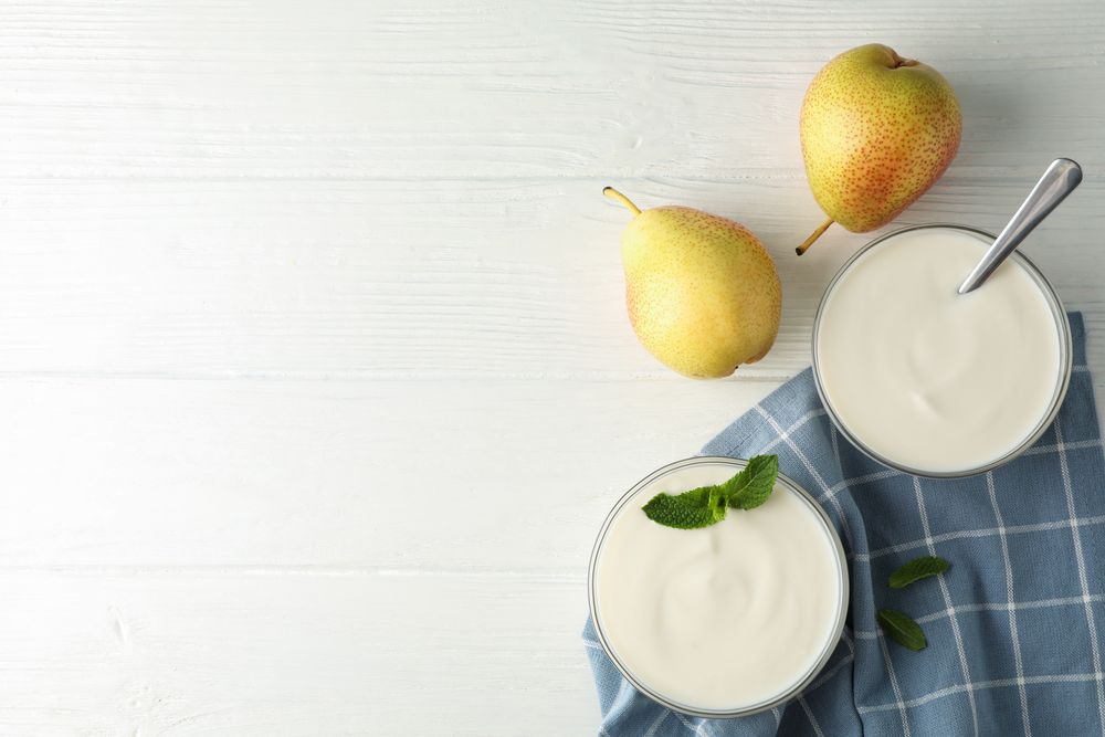 Cream yogurt, pears, towel and mint on wooden background, top view