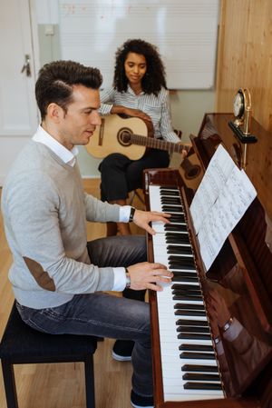 Man playing piano near woman playing guitar in studio