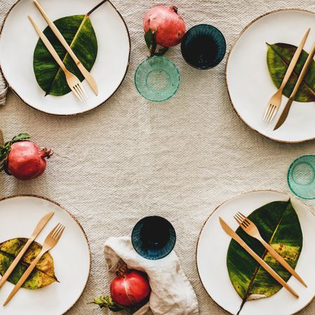 Fresh table setting on brown table cloth, leaves on bright plates, fruit, glassware, square crop