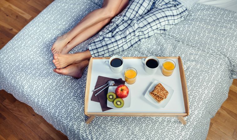 Healthy breakfast on tray and couple legs over bed