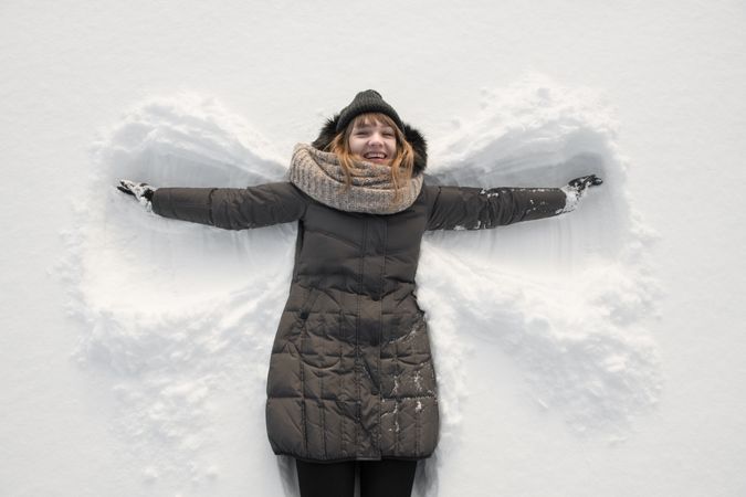 Woman in winter wear making snow angel