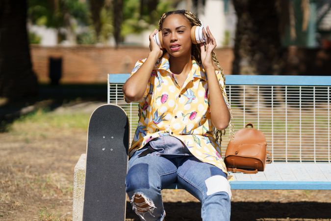 Female in bold patterned shirt on park bench listening to music on large headphones