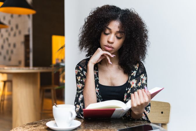 Black woman reading book at cafe table