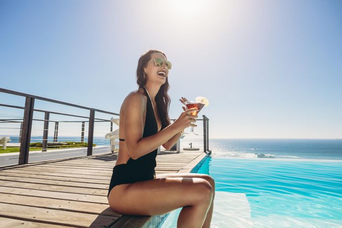 Female model enjoying a summer day at the resort swimming pool near the ocean