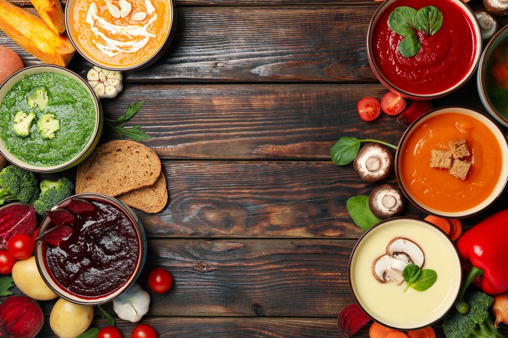 Top view of colorful soups lined up on both sides of dark wooden table with copy space