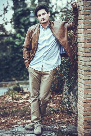 Man in khakis and button up shirt leaning on brick wall on autumn day