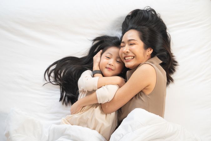 Top view of Asian mother and daughter cuddle and talking on bed.