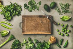 Arrangement of fresh green garden vegetables on concrete surface, with wooden board