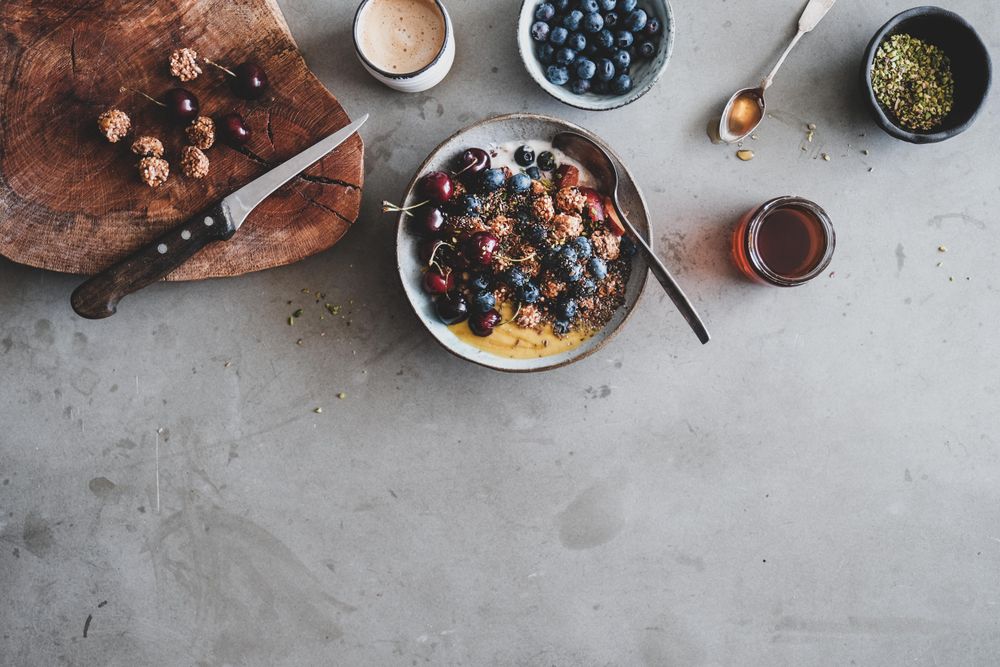 Oat granola yogurt bowl with cherries, blueberries, honey, nuts, coffee, wooden board