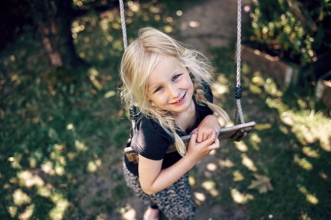 Blonde girl with braided hair playing on outdoor swing in backyard