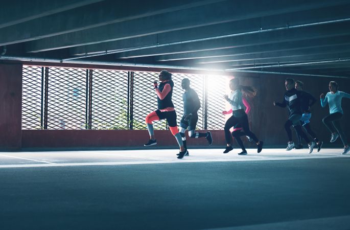 Group of people running in an industrial building next to a window with light shining in