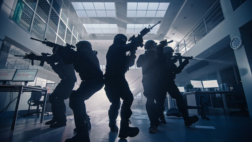 Masked Team of Armed SWAT Police Officers Move in a Hall of a Dark Seized Office Building with Desks and Computers.