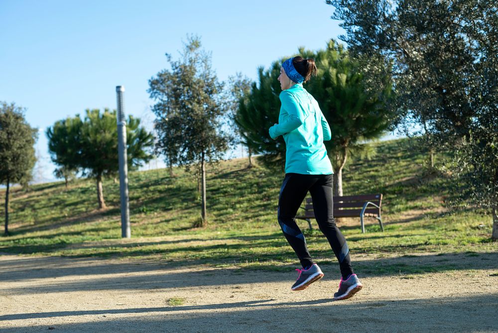Back of woman in ear warmers jogging outdoors on sunny fall day