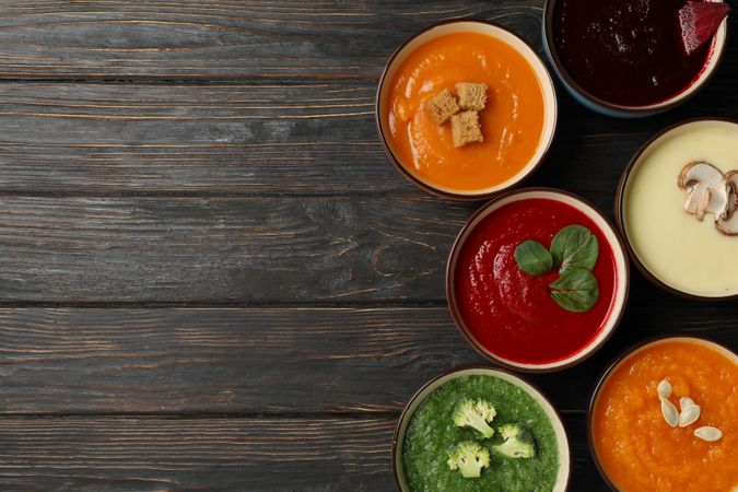 Top view of colorful fall soups lined up on right of dark wooden table with copy space