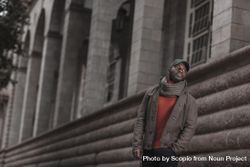 Man in brown jacket  and scarf standing beside a building 4Aoym0