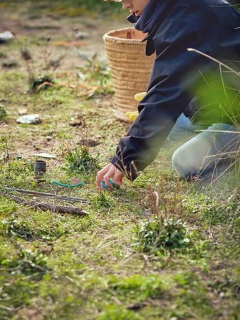 Crop preteen boy picking garbage on grassy ground in countryside