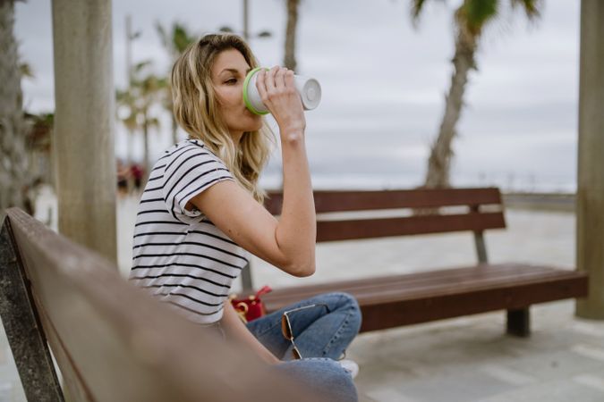 Happy woman with disposable cup of coffee sitting on street bench