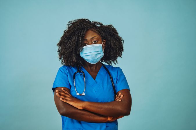 Black female doctor standing with arms crossed with face mask and stethoscope