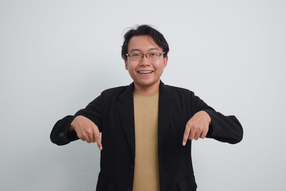 Joyful Asian businessman with suit and casual shirt pointing down