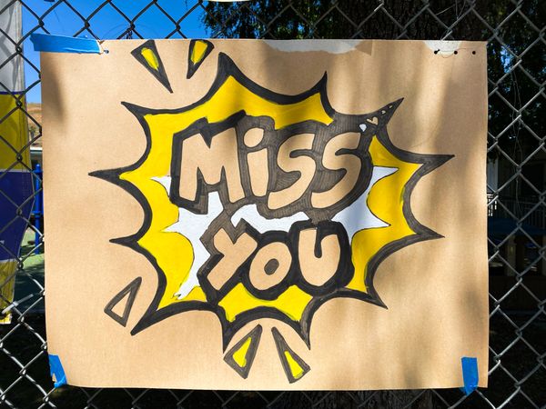 Close up shot of brown sign taped to school fence with the words “miss you”