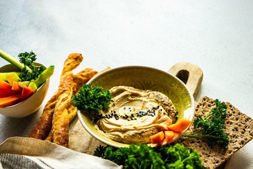 Traditional hummus dip in bowl on board served with veggies and rye crackers