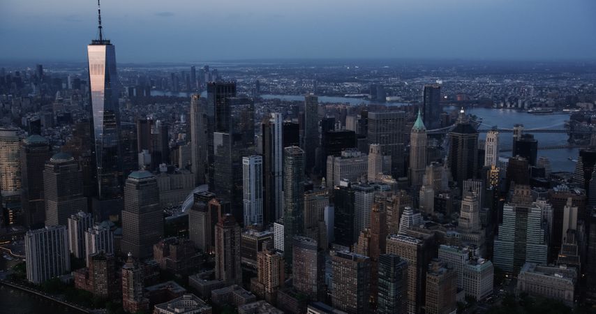 Evening Panorama Around the Wall Street Financial District in New York City, USA. Dark Aerial Photo with Lit Office Buildings and Skyscrapers on a Summer Night with Deep Blue Sky