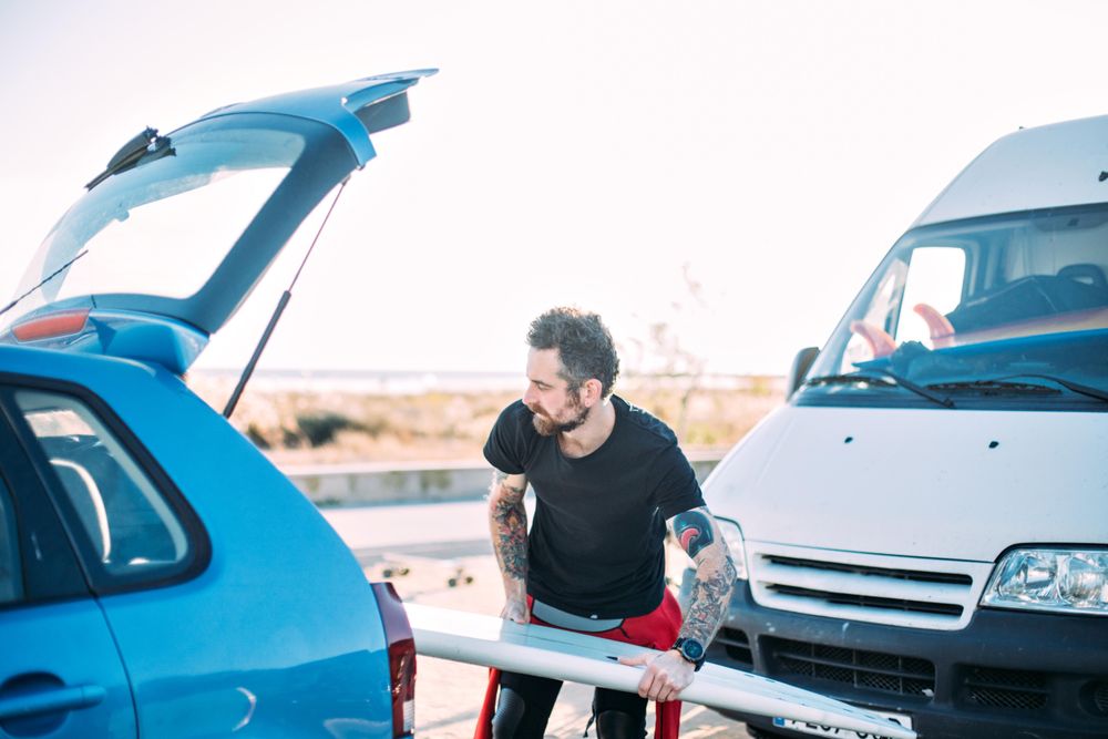 Man loading surfboard into vehicle