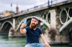 Satisfied male tourist taking selfie on smartphone at quay