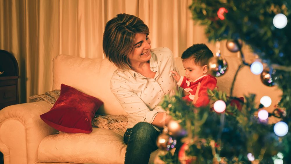 Mother playing with baby near Christmas tree