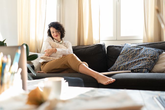 Woman with pillow on sofa near table with brushes and laptop