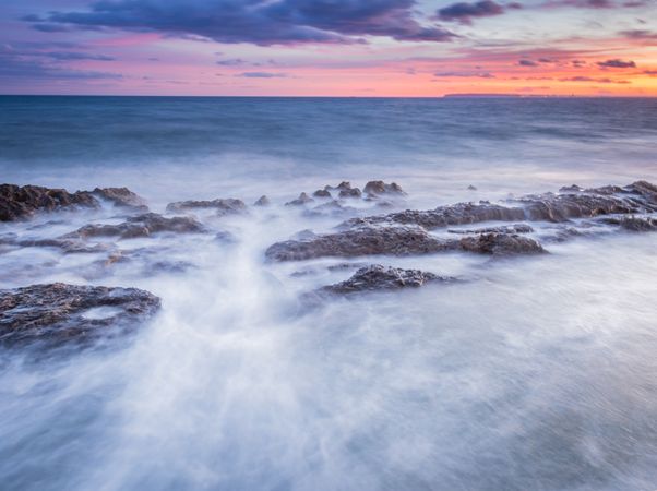 Sea waving near rough rocks during sunset
