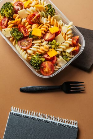 Lunchbox with pasta and plastic fork by notepad and pencils