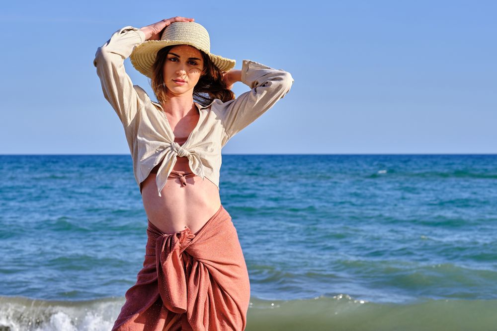 A fashion model with a hat at the beach before sunset