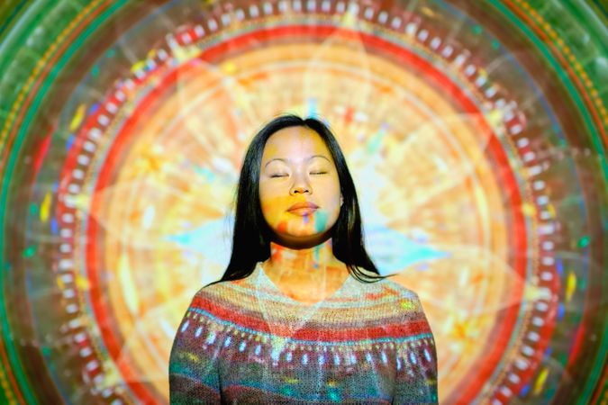 Peaceful Asian woman doing yoga near glowing mandala
