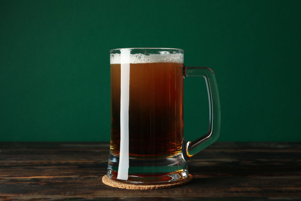 Glass of beer on wooden table against green background
