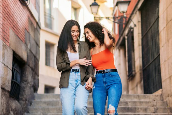 two young women walking down street stairs smiling holding her hands