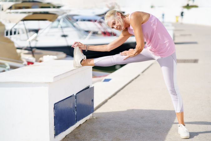 Older female in pink athletic wear stretching her legs after workout