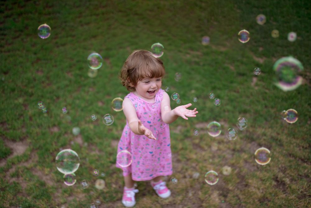 Joyful girl playing with colorful bubbles in grass