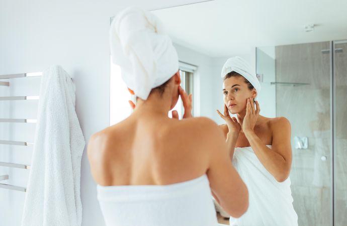 Woman observing her face in mirror in bathroom