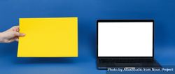 Mockup laptop screen with hands holding yellow paper next to it for copy space 5oJpG0