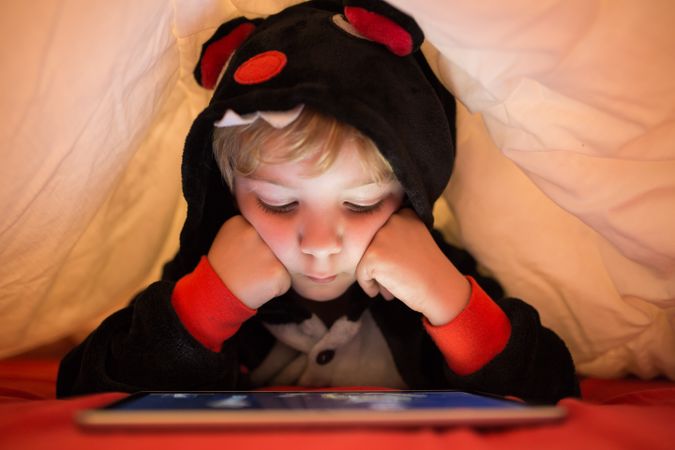 Boy using tablet under blanket