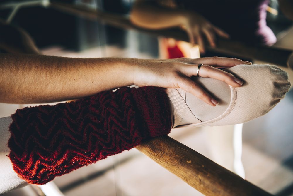 Crop shot of female leg in pointe shoe on barre stretching in studio.