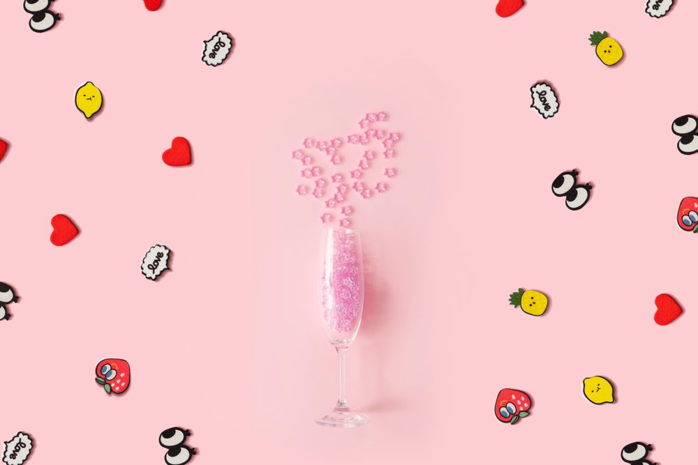 Champagne flute with pink plastic stars on pastel pink background with pop art stickers