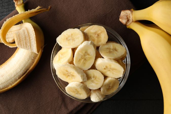Bowl of banana slices, banana and towel on wooden background