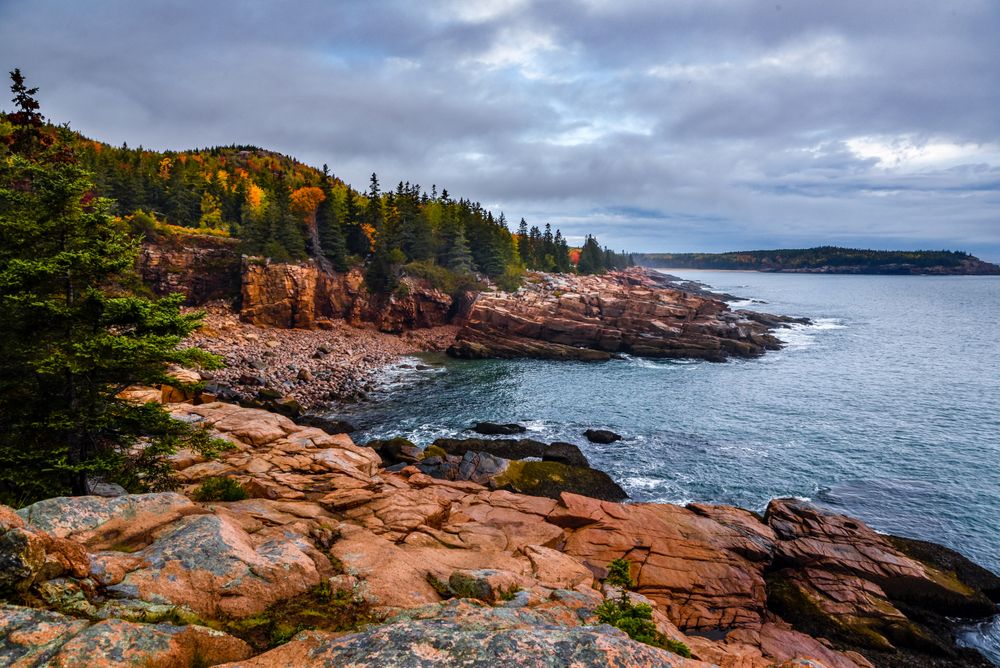 Green and brown mountain beside ocean under cloudy sky