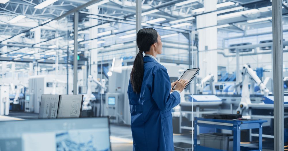 Factory Chief Technical Officer Working on Tablet at Futuristic Industrial Manufacture with Autonomous Robotic Assembly Line. Specialist Monitoring Production, Planning Work for Employees