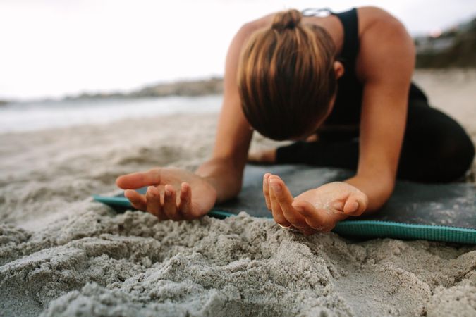 Close up of a woman sitting on mat at the beach practicing yoga