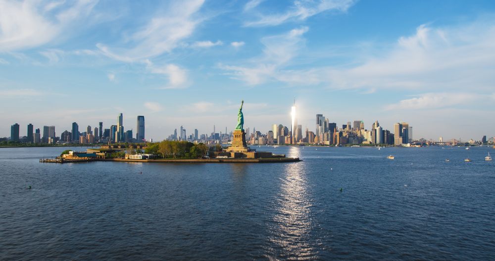 Aerial Helicopter Cinematic Passing View of the Statue of Liberty with Manhattan Skyline Cityscape. Panoramic View of New York City Skyscrapers and Jersey City Buildings on a Sunny Day