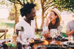 A man and woman laughing and smiling sitting at an outdoor lunch table with a smartphone a0LrD4