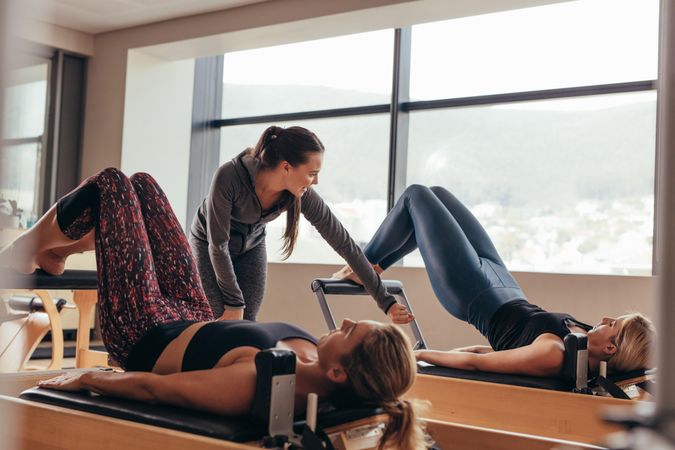 Two fitness women being trained by pilates instructor